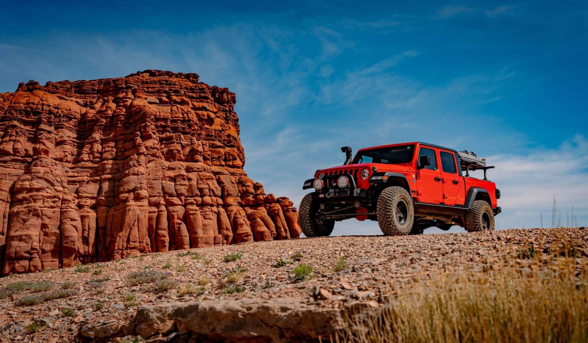 Red Jeep Gladiator on Moab red rock under blue sky